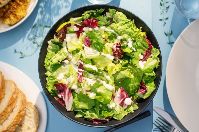 Salaattikulho jossa Hetki-salaatinkastiketta, taustalla leipää ja kanaa